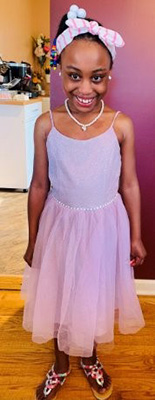 Young girl wearing a pink dress and smiling.