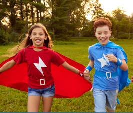 Two children running while wearing colorful capes