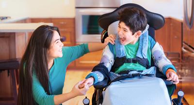 Disabled boy in wheelchair laughing with teen sister in kitchen