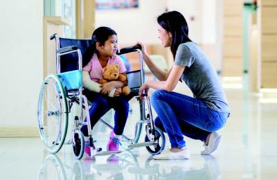 Girl in a wheelchair looking at her mom kneeling beside her.