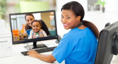 Health care provider smiles as parent and child are visible on the computer screen in front of them