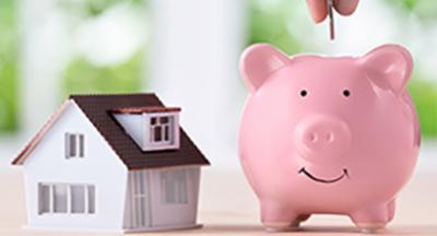 A minature house sitting next to a pink piggy bank